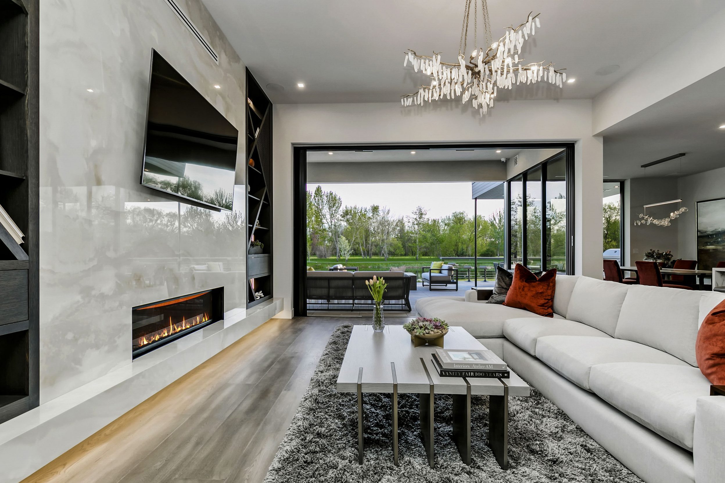 Modern living room with high contrast detail, light gray marble fireplace with built in shelving. Open sliding glass doors reveal a luxurious back patio with views of the water at Renovare in Eagle, Idaho