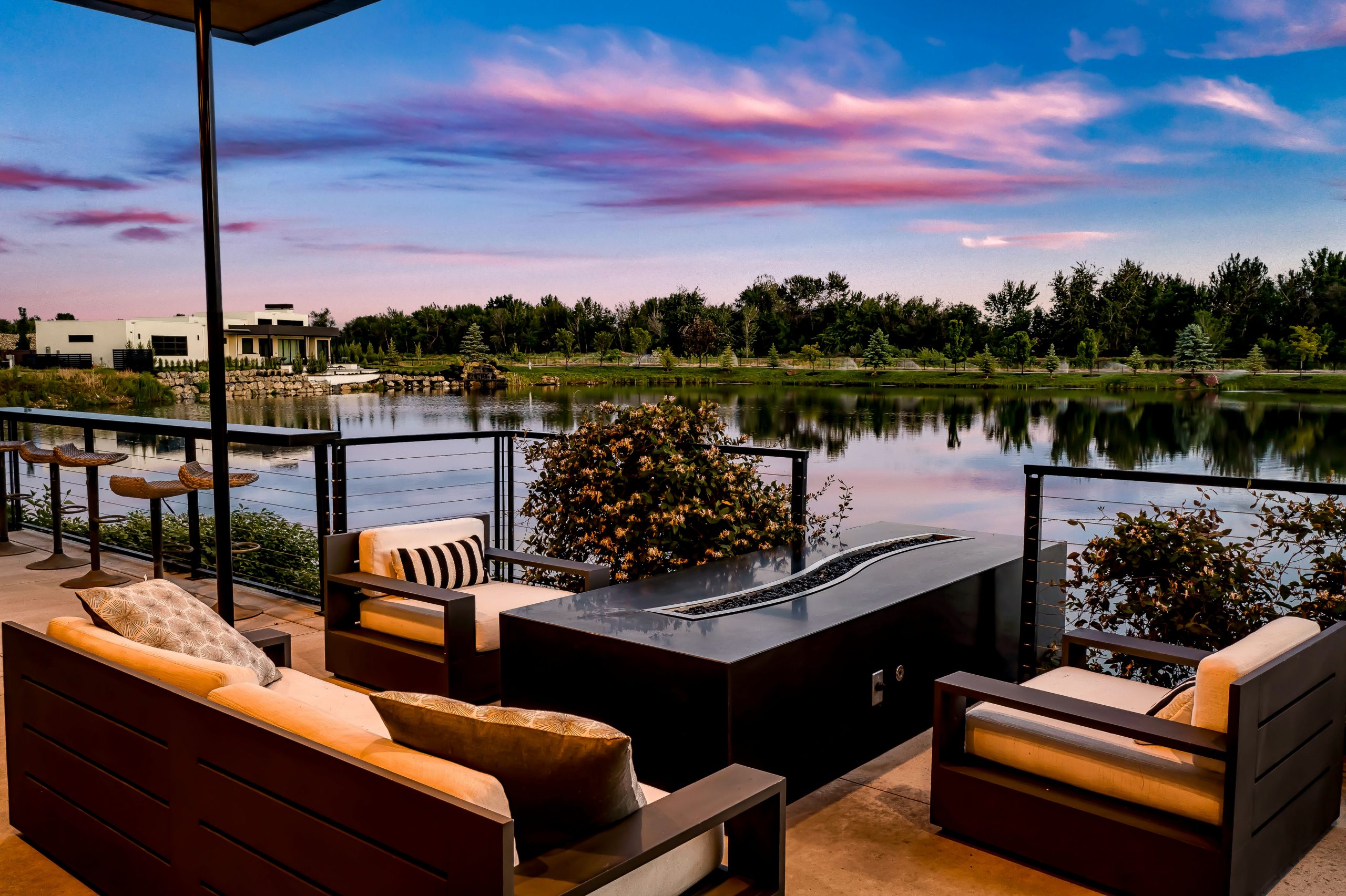 Outdoor couches and firepit table overlooking the water at Renovare in Eagle. Sunset sky and lush landscpaing reflect off the water